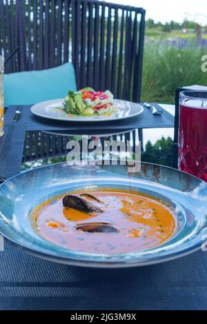 Köstliche Meeresfrüchte Tomatensoße mit Bouillabaisse Fischsuppe mit Garnelen, Muscheln und Fisch auf einem blauen Teller auf dem Tisch. Köstliches romantisches Abendessen in einer Fischruhe Stockfoto