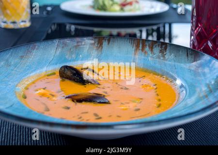 Köstliche Meeresfrüchte Tomatensoße mit Bouillabaisse Fischsuppe mit Garnelen, Muscheln und Fisch auf einem blauen Teller auf dem Tisch. Köstliches romantisches Abendessen in einer Fischruhe Stockfoto