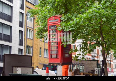 London, Großbritannien. 7.. Juli 2022. Arbeiter entfernen eine alte, zerbrochene rote Telefonbox im Londoner West End. Stockfoto