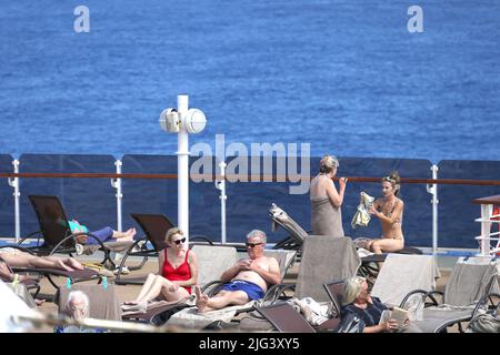 Massen von reifen Passagieren entspannen sich auf einem sonnigen Kreuzfahrtdeck, während die Industrie nach der Coronavirus-Pandemie langsam wieder in den normalen Betrieb zurückkehrt. Stockfoto