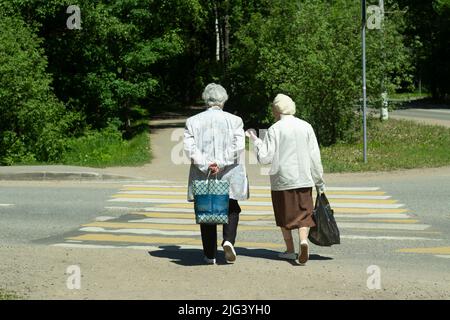 Zwei alte Frauen gehen über die Straße. Rentner in Russland. Die alten Damen überqueren die Straße. Stockfoto