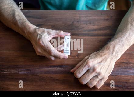 Nahaufnahme eines Mannes mit einem besorgten Antigen-Testkit mit dem Ergebnis von 2 Streifen. Der mit dem Coronavirus infizierte Patient fühlt sich nach der Überprüfung der Position gestresst Stockfoto