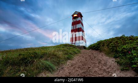 Leuchtturm auf einer Sanddüne mit Leymus. Ein Sandfleck führt zum Leuchtturm hinauf. Aufgenommen während der blauen Stunde in Vorupør, Dänemark. Stockfoto