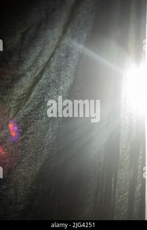 Lichtstrahlen auf Stoff. Erneutes Ausleuchten des Rahmens. Die Dämmerung durch Vorhänge am Fenster. Stockfoto