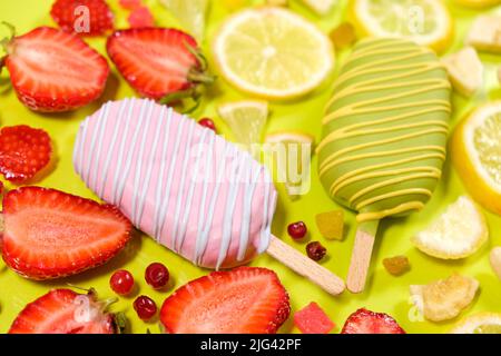 Zwei Eiscremes auf einem Stock - Erdbeere und Zitrone auf gelbem Hintergrund. Sommerliche Fruchtdesserts. Stockfoto