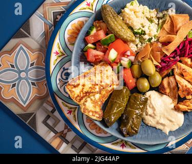 Eine Portion traditioneller östlicher mediterraner arabischer Speisen wie Hummus, Oliven, gegrilltes Huhn, Halloumi, Dolma, Couscous, Salat und pickl Stockfoto