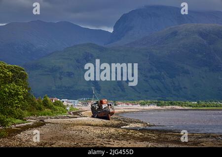 Ein zerstörtes Fischerboot am Ufer des Loch Linhe, dem Dorf Caol und Ben Nevis dahinter, von Corpach auf dem Caledonian Canal, West Schottland Stockfoto