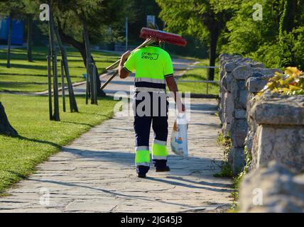 Ein männlicher Straßenputzer, der eine Bürste und eine Tasche trägt und in der frühen Morgensonne von Santander Cantabria aus gesehen geht Stockfoto