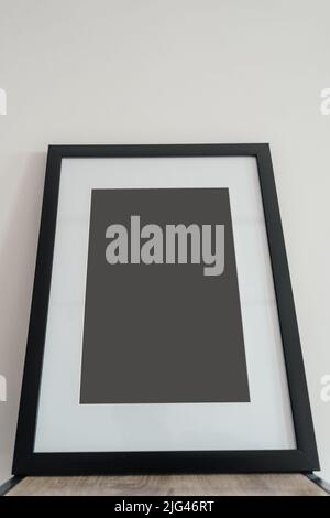 Im Innenraum steht ein leerer Bilderrahmen aus Holz auf weißem Hintergrund. Mockup-Posterrahmen. Stockfoto
