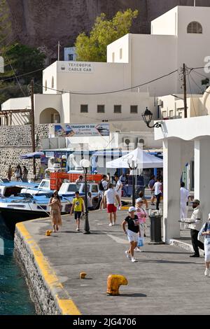 Fira, Santorini, Griechenland - 2022. Juni: Menschen, die am Hafen spazieren. Im Hintergrund befindet sich die Seilbahnstation am Fuße der Klippe Stockfoto