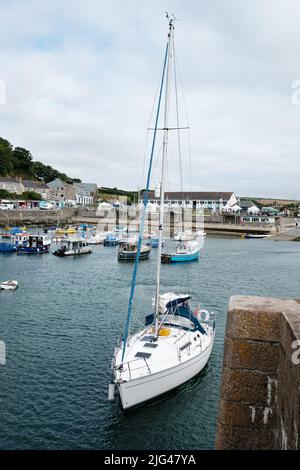 Eine Yacht, die den Hafen von Porthleven, Cornwall verlässt Stockfoto