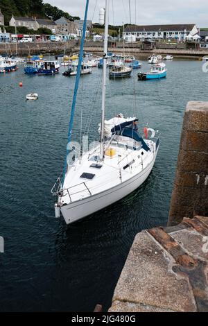 Eine Yacht, die den Hafen von Porthleven, Cornwall verlässt Stockfoto