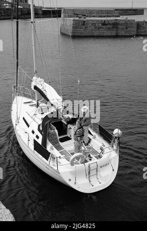 Eine Yacht, die den Hafen von Porthleven, Cornwall verlässt Stockfoto