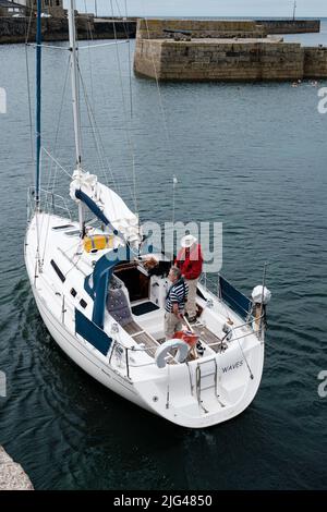 Eine Yacht, die den Hafen von Porthleven, Cornwall verlässt Stockfoto