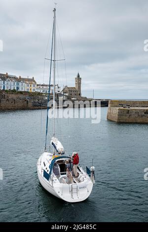 Eine Yacht, die den Hafen von Porthleven, Cornwall verlässt Stockfoto