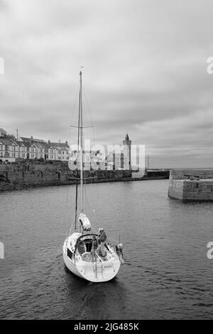 Eine Yacht, die den Hafen von Porthleven, Cornwall verlässt Stockfoto