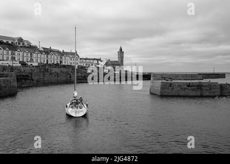 Eine Yacht, die den Hafen von Porthleven, Cornwall verlässt Stockfoto