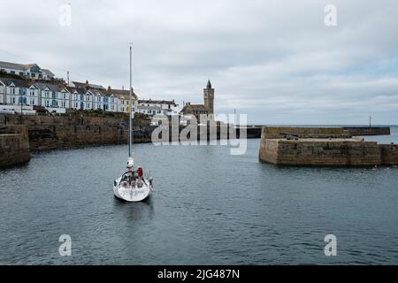 Eine Yacht, die den Hafen von Porthleven, Cornwall verlässt Stockfoto