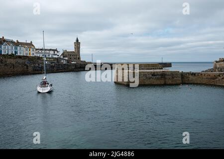 Eine Yacht, die den Hafen von Porthleven, Cornwall verlässt Stockfoto
