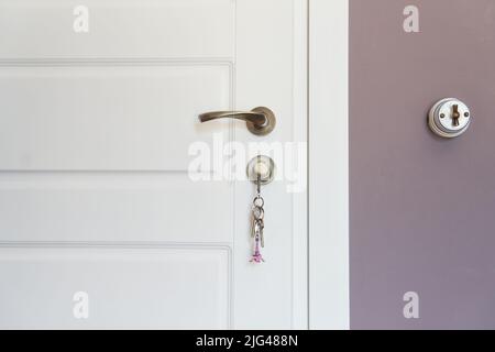 Teil einer weißen, modernen Innentür mit Schlüssel im Schloss und Metallgriff Stockfoto