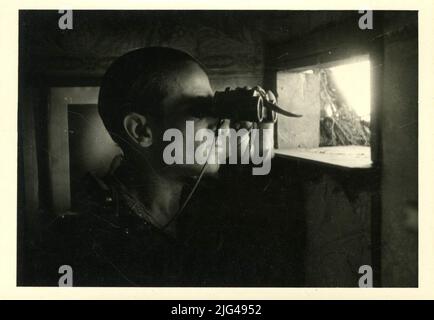 Porträt des Divisionären Soldaten mit Prismatic. Innenportrait eines Divisionssoldaten mit einem Fernglas an einer hinter ihm liegenden Tronera, an der Wand, ein Propagandafoto von Adolf Hitler Stockfoto