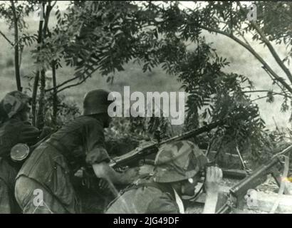MG-34 Maschinengewehr ausgefallen. Drei Divisionäre in einem Graben mit einem leichten Maschinengewehr Schuss MG-34, beobachtet eine vierte Figur mit prismatischem, trägt einen Unterfusil MP 40. Sie tragen einen Helm M 35, zwei davon mit verstellbaren Stoffbezügen. Stockfoto