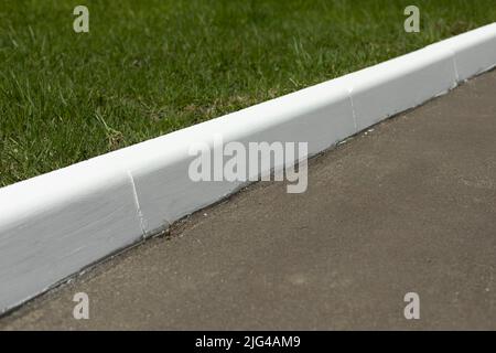 Weißer Bordstein auf der Straße. Landschaftsgestaltung im Park. Lackierter Bordstein. Stockfoto