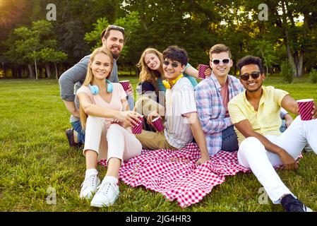 Portrait einer Gruppe von glücklichen Freunden, die sich auf einem kleinen improvisierten Picknick im Park entspannen. Stockfoto