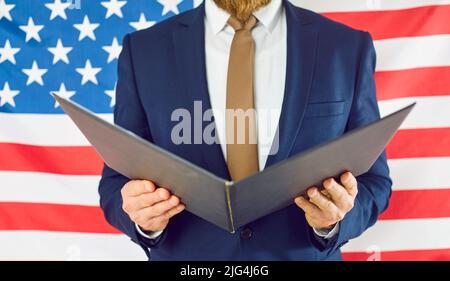 Nahaufnahme eines offenen Ordners in den Händen eines unbekannten Mannes im Anzug auf dem Hintergrund einer amerikanischen Flagge. Stockfoto