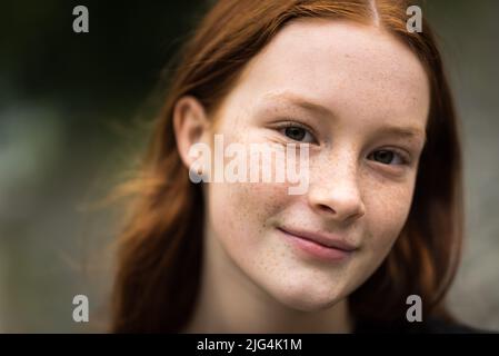 Rothaarige 12-jährige Mädchen mit Sommersprossen posiert mit einem Stadt Bokeh Hintergrund, Jette, Belgien Stockfoto