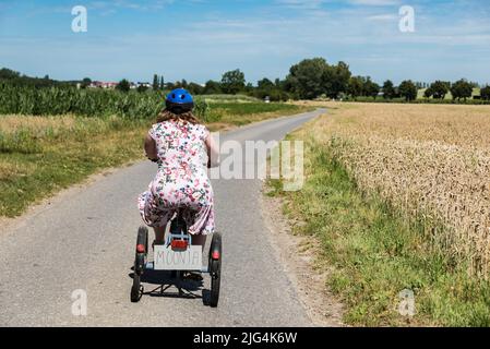 Junge Frau mit Down-Syndrom fährt auf einem Dreirad durch die Felder auf dem belgischen Land, Belgien Stockfoto