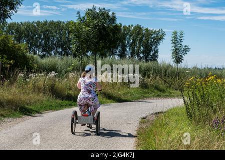 Junge Frau mit Down-Syndrom fährt auf einem Dreirad durch die Felder auf dem belgischen Land, Belgien Stockfoto