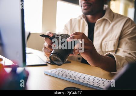 Junger Schwarzer Professioneller Fotograf, Der Am Schreibtisch Sitzt Und An Der Kamera Arbeitet, Die Bilder Bearbeitet Stockfoto