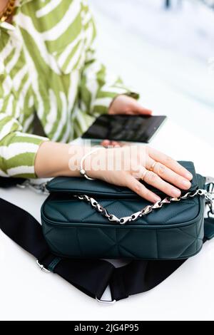 Die Hand einer Frau liegt auf einer kleinen schwarzen Handtasche auf dem Tisch Stockfoto