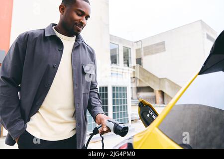 Mann, Der Elektroauto Vor Dem Büro Im Parkplatz Ansteckt, Lädt Stockfoto