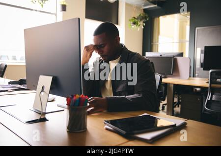 Gestresster schwarzer Geschäftsmann saß mit einer psychischen Erkrankung am Schreibtisch Stockfoto