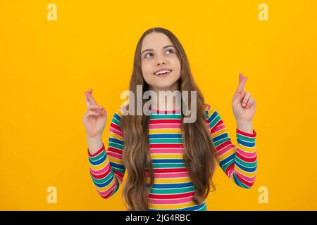 Zufrieden fröhlich Teenager Kind wünscht viel Glück, kreuzt die Finger, hat Vertrauen für besser, isoliert über gelben Hintergrund. Stockfoto