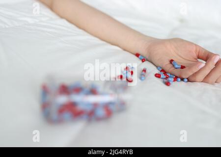 Frau Hand nach Überdosis von medizinischen Pillen auf dem Bett Stockfoto