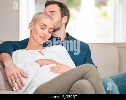 Eine Familie gründen. Eine kurze Aufnahme eines anhänglichen jungen, erwartungsvollen Paares, das zu Hause auf dem Sofa sitzt. Stockfoto