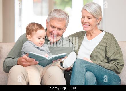 Zeit mit Oma und Opa verbringen. Eine kurze Aufnahme eines liebevollen älteren Ehepaares, das ihrem Enkel vorlas, während er zu Hause auf dem Sofa saß. Stockfoto