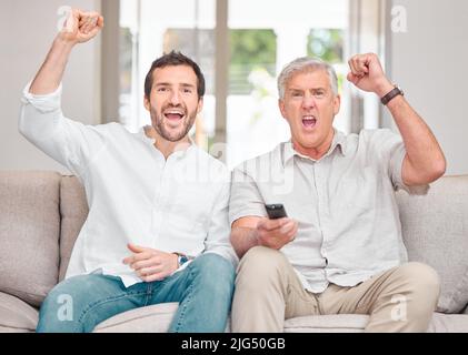 Komm schon. Beschnittenes Porträt eines hübschen jungen Mannes und seines älteren Vaters, der ihr Team anfeuert, während er zu Hause auf dem Sofa Sport sieht. Stockfoto