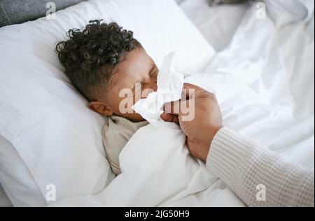 Nun versuchen Sie, damit Sie sich besser fühlen. Kurzer Schuss einer Frau, die ihrem Sohn hilft, sich die Nase zu blasen, während sie sich krank fühlt. Stockfoto