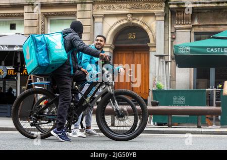 Zwei Deviveroo-Fahrradlieferer halten für ein freundliches Gespräch auf der Castle Street in Liverpool Stockfoto