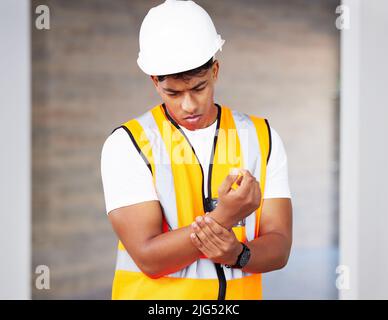 In dieser Branche setzen wir uns durch. Aufnahme eines jungen Auftragnehmers mit Schmerzen am Handgelenk. Stockfoto