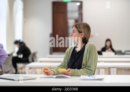 Gelangweilt oder müde von der Studie weibliche reife Studentin Blick auf Fenster mit frustrierten Gesichtsausdruck Stockfoto