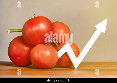 Der Preis für Tomaten und Gemüse. Steigende Preise für Tomaten. Frische rote reife Tomaten mit Zweigen auf dem Tisch. Das Diagramm zeigt nach oben Stockfoto