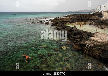 Lanzarote, Spanien. 07.. Juli 2022. Ein Mann schnorchelt im kristallklaren türkisfarbenen Wasser, während sich einige Leute an einem Sommertag in den natürlichen Pools von Punta Mujeres abkühlen. Punta Mujeres ist ein kleines Dorf im Nordosten der Vulkaninsel Lanzarote. Quelle: Marcos del Mazo/Alamy Live News Stockfoto