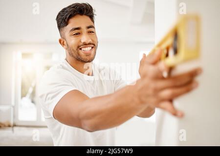 Ich mache die Arbeit lieber selbst. Aufnahme eines hübschen jungen Mannes, der allein in seinem Haus steht und mit einem Lineal eine Mauer misst. Stockfoto