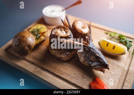 Nahaufnahme von geröstetem Makrelenfisch mit Zitrone, Kartoffel und Sauce auf Holzbrett Stockfoto