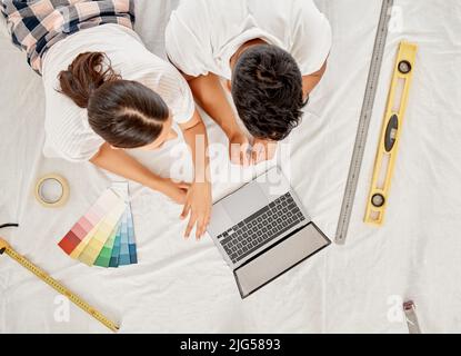 Inspiration holen. Ein unverkennbares Paar, das auf dem Boden des Wohnzimmers liegt und einen Laptop verwendet, wurde aus einem hohen Winkel aufgenommen. Stockfoto